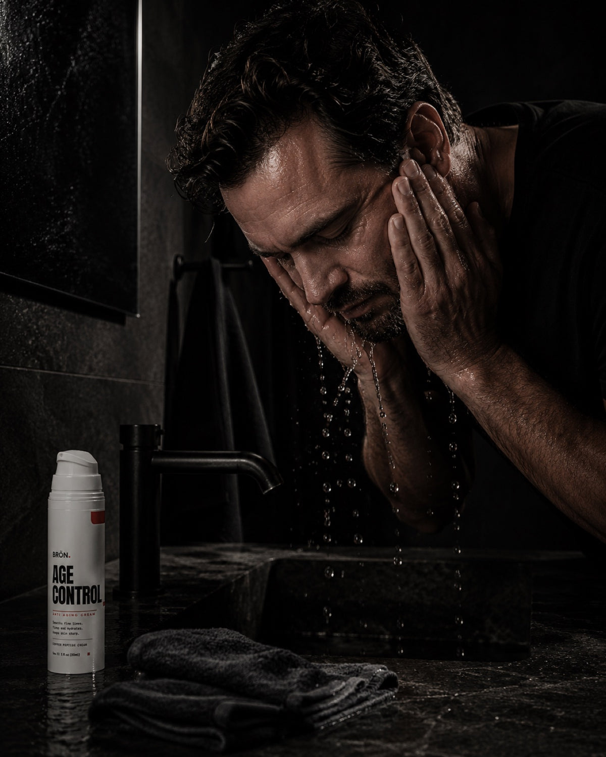 Man splashing water on his face at a dark bathroom sink