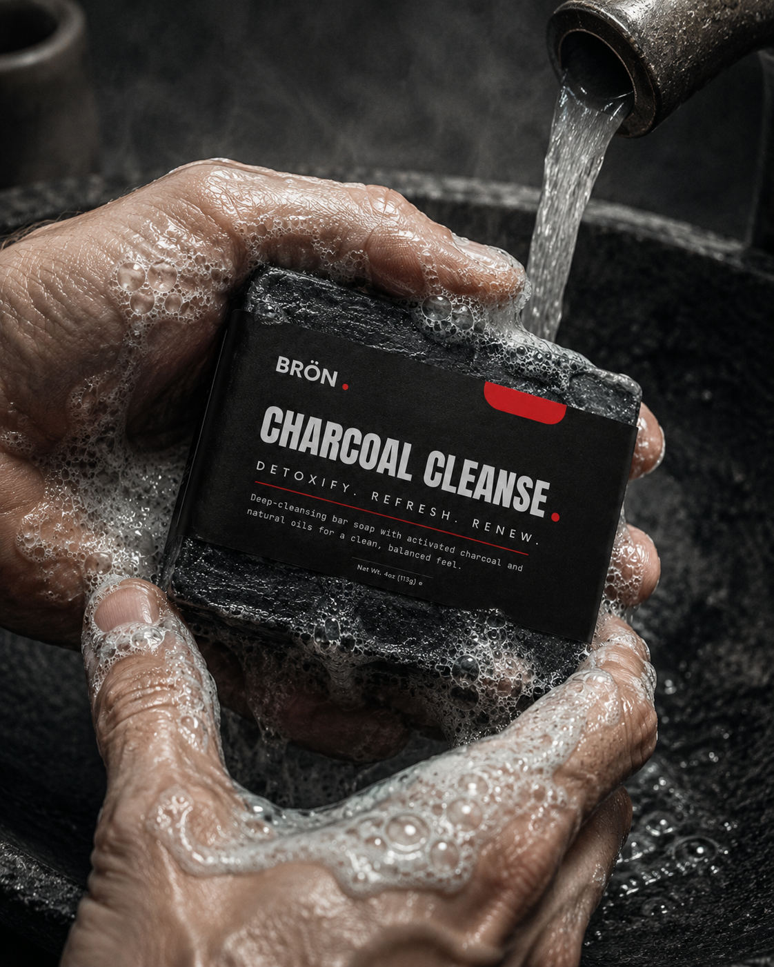 Hands rolling the charcoal soap bar into thick lather under running water