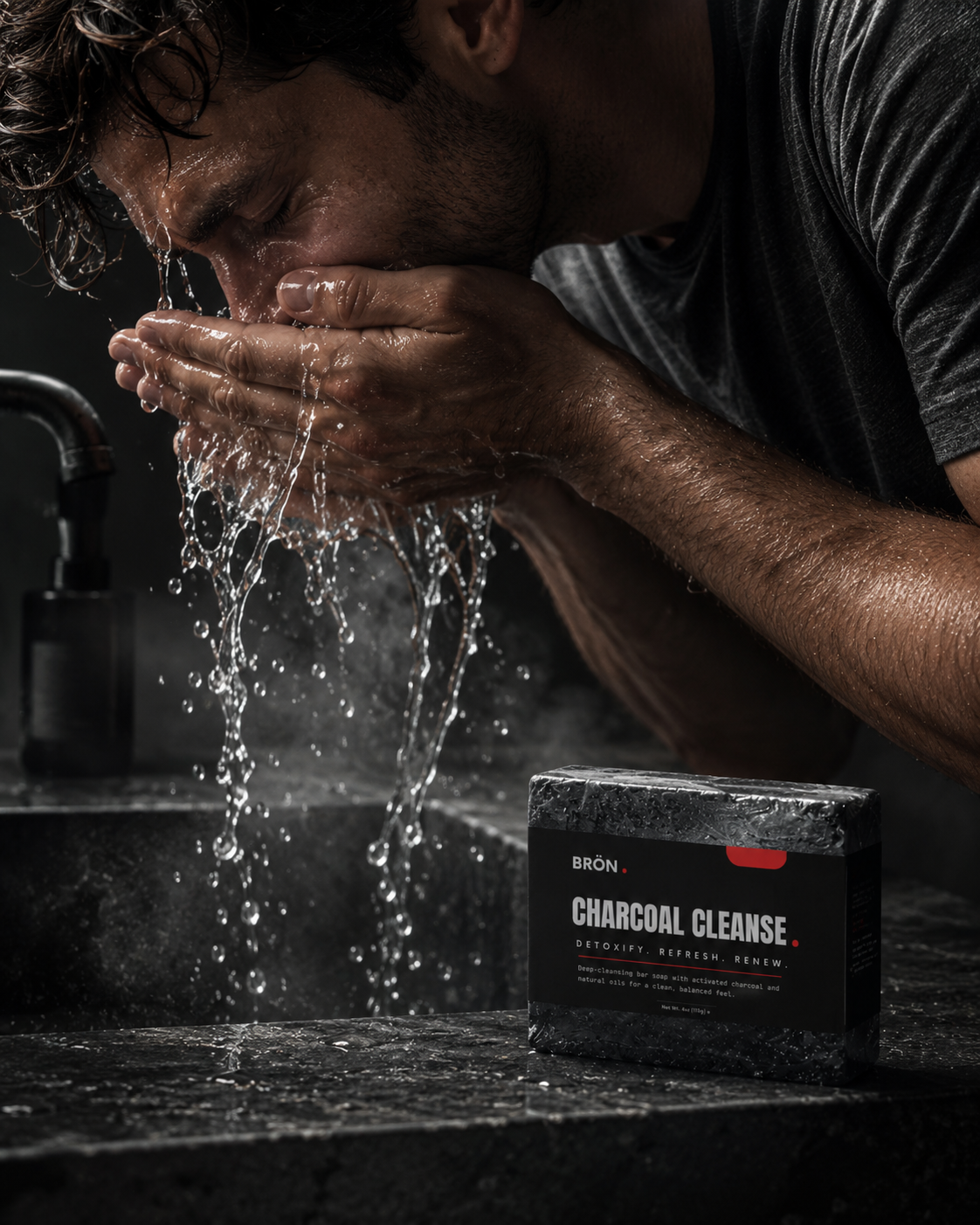 Man splashing warm water on his face at a dark stone sink, the charcoal soap bar beside the faucet