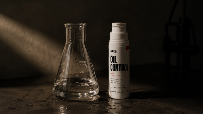 Lab beaker beside the BRON Oil Control bottle on a dark surface
