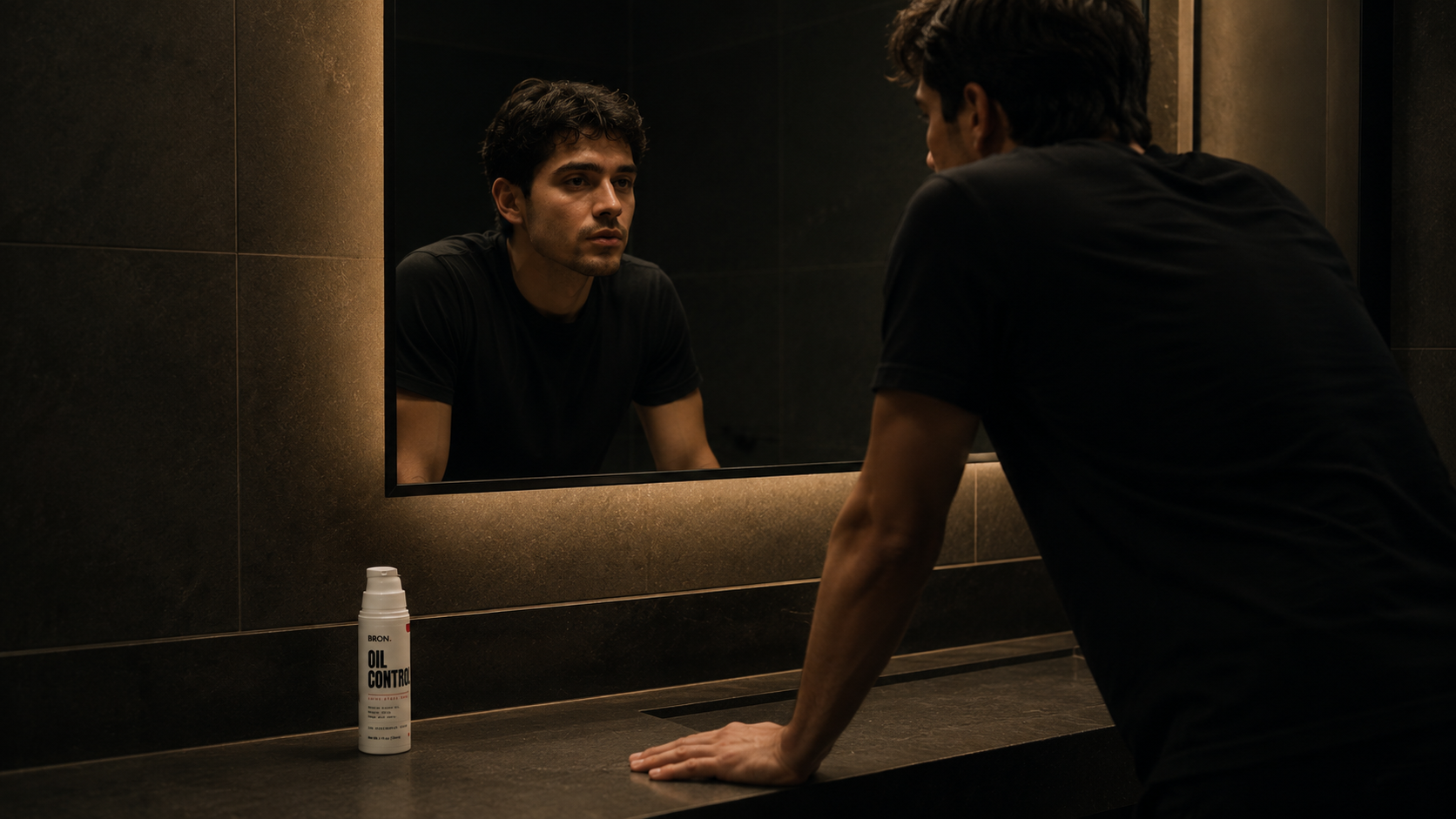 Man at a dark bathroom mirror, BRON Oil Control on the counter